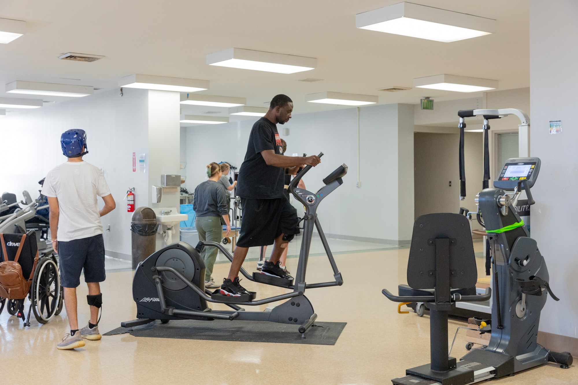 Patient in black shirt using elliptical in Med Rehab Adult Gym
