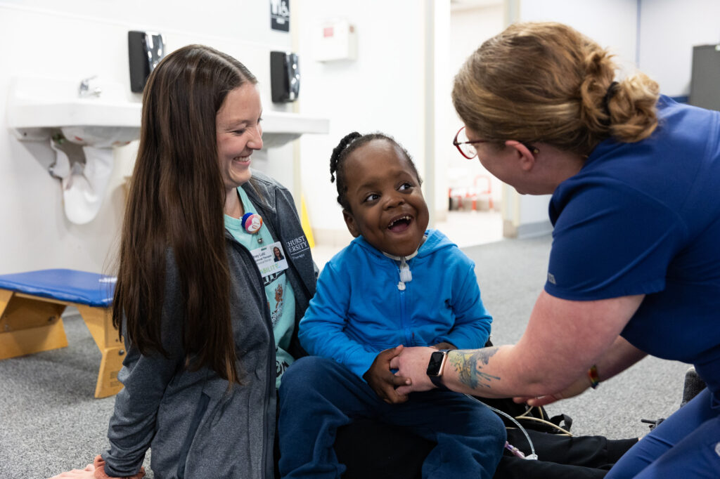 Pediatric patient in blue smiling with two therapists