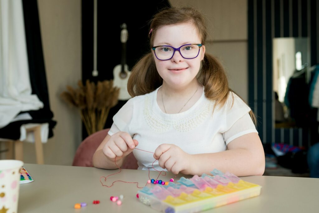 teen girl stringing beads and making bracelet. Down syndrome kid crafting jewelry and threading bead