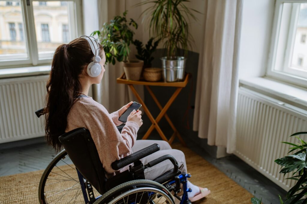 Unhappy teenage girl sitting on a wheelchair and looking out of the window.